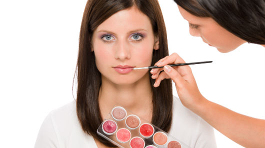 Maquiadora passando batom em sua cliente com pincel
